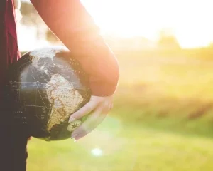 Une personne tient un globe terrestre à la main et au fond il y a une église